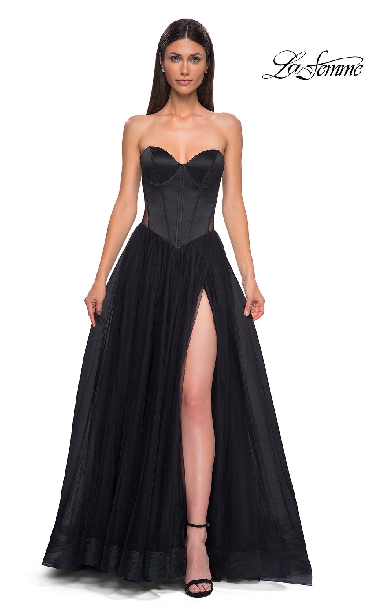 A woman wears the Black Strapless Long Prom Dress: La Femme 32771, featuring a sweetheart neckline, corset-style bodice, and high side slit, standing against a white background with the